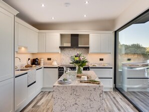 A modern kitchen with marble countertops, a central island, and a view through a glass door.