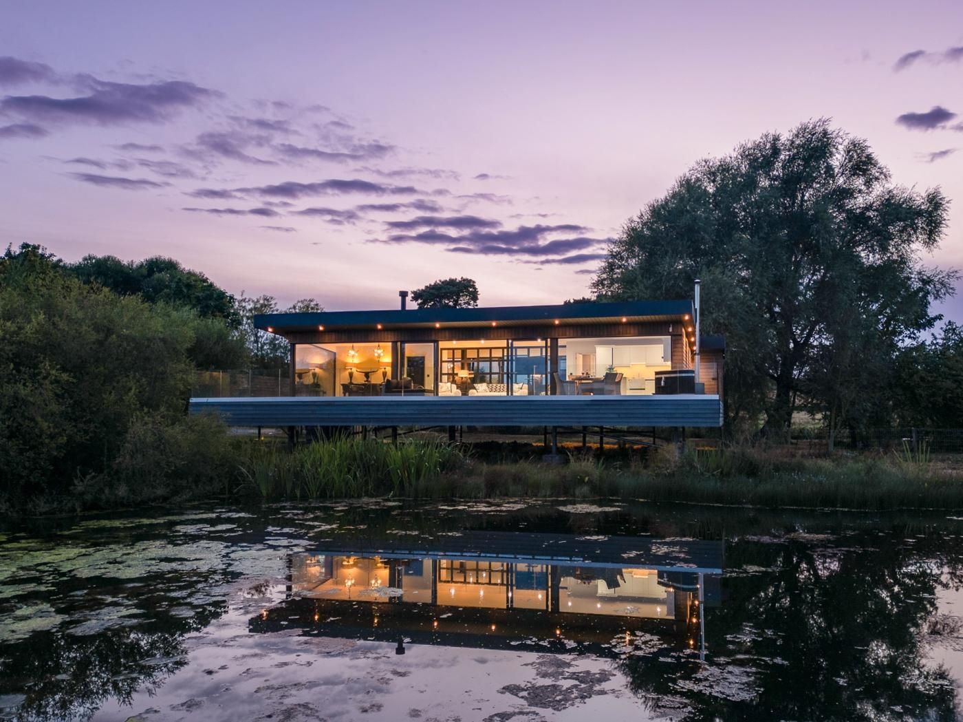 Una casa moderna con fachada de vidrio, ubicada junto a un cuerpo de agua con reflejos.