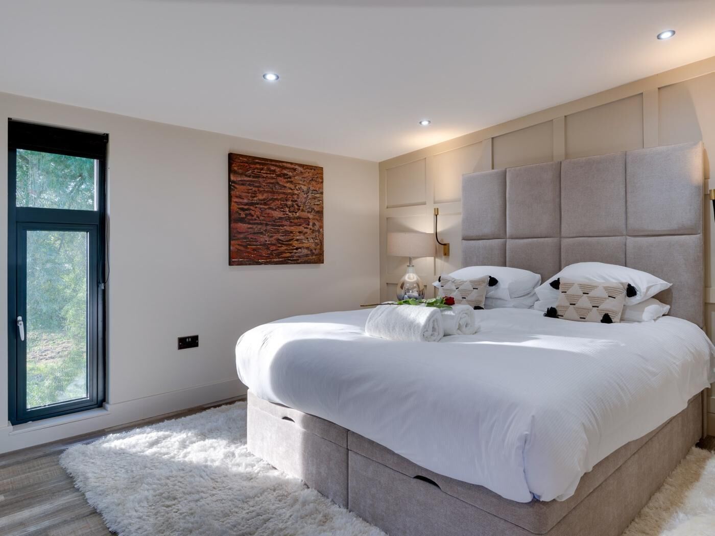 A modern bedroom with a large bed, a window, and a painting on the wall.