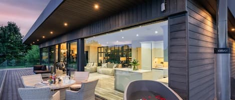 A modern outdoor living area with a hot tub, wicker furniture, and a view of the interior.
