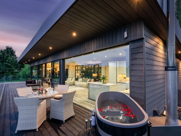 A modern outdoor living area with a hot tub, wicker furniture, and a view of the interior.