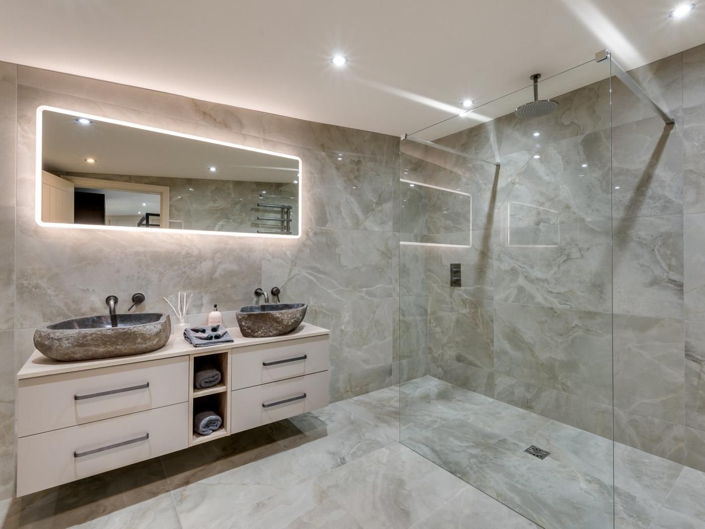 Un baño moderno con lavamanos de mármol, cabina de ducha de vidrio y un espejo grande con iluminación integrada.