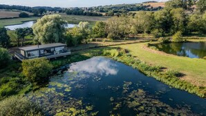 Uma casa moderna com fachada de vidro, rodeada por um lago e vegetação exuberante.