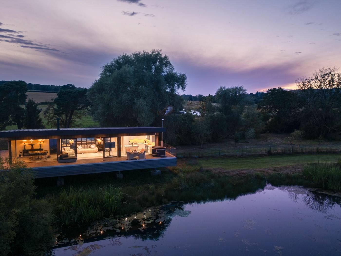 A modern house with a glass facade, a deck, and a pond in the foreground.