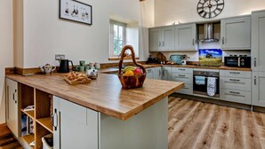 Una cocina moderna con una isla de madera, armarios grises, un reloj grande y un ventanal.