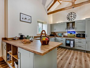 A modern kitchen with a wooden island, grey cabinets, a large clock, and a window. - 4 Bed in Spennymoor (oc-95189) (Byers Green)