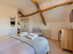 Ein Schlafzimmer mit einem Bett, einem Sessel, einem Schminktisch, einem Spiegel und einem Holzbalken an der Decke.