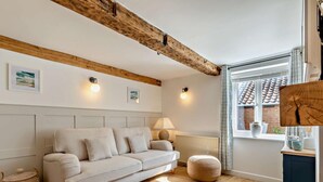 Una sala de estar acogedora con un sofá, una lámpara, un ventanal con vistas y una viga de techo de madera.