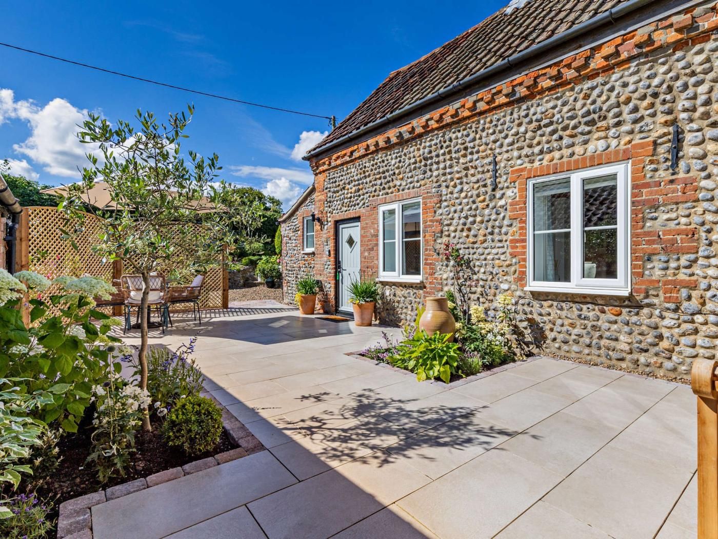 Une maison en pierre avec un patio carrelé, une clôture en bois et des plantes en pot.