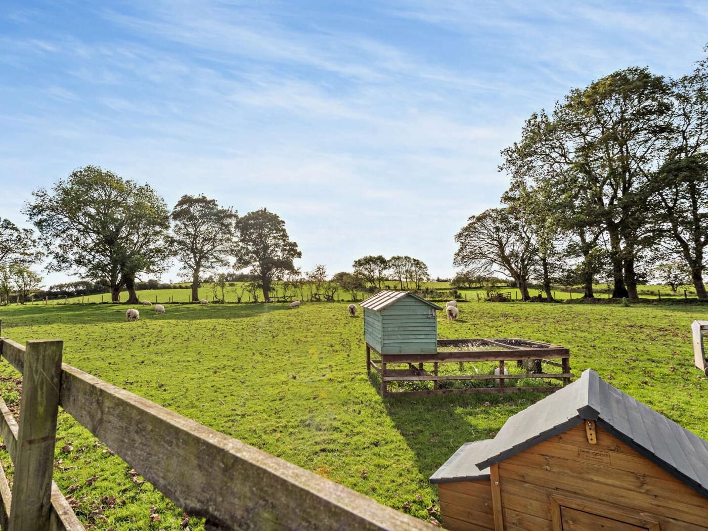 A rural landscape with a green field, a wooden fence, and a small wooden structure.