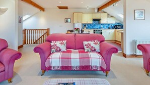 Ein gemütliches Wohnzimmer mit einem rosa Sofa, einem Esstisch und einer Küche im Hintergrund.