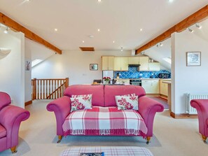 Ein gemütliches Wohnzimmer mit einem rosa Sofa, einem Esstisch und einer Küche im Hintergrund.