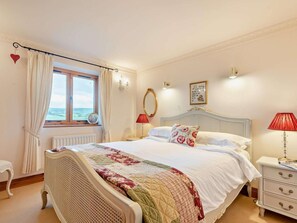 Ein Schlafzimmer mit einem Bett, einem Fenster, einem Nachttisch und einer Lampe.