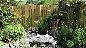A garden patio with a table and chairs, surrounded by plants and a wooden fence. - 1 Bed in Keswick (oc-87483) (Applethwaite)