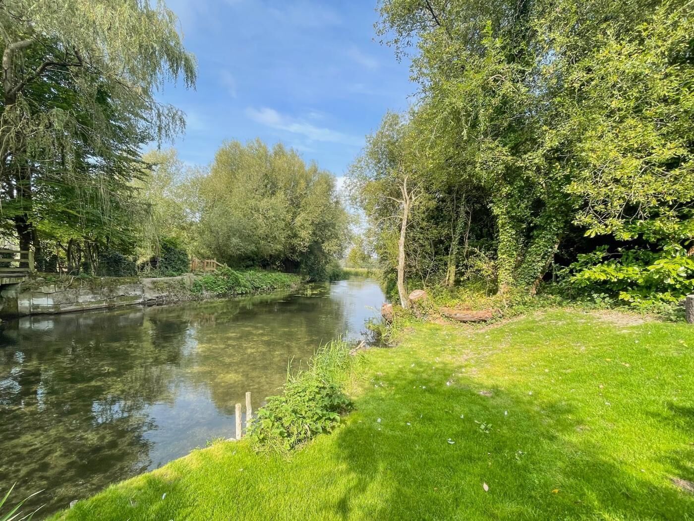 A river with trees on both sides, a grassy bank, and a wooden structure.