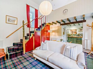 A living room with a sofa, a staircase with red steps, a kitchen in the background, and a clock on the wall. - 6 Bed in Penrith (oc-95344) (Ullswater)