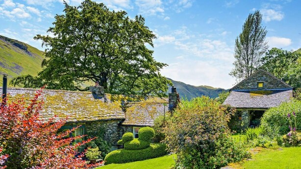 Une charmante maison en pierre avec un toit de chaume, entourée d’un jardin bien entretenu, agrémenté d’un labyrinthe de haies et d’un petit ruisseau.
