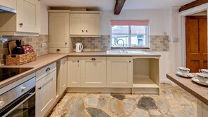 A kitchen with stone flooring, a window with a view, and a wooden ceiling beam. - 2 Bed in Exeter (oc-93129) (Crediton Hamlets)