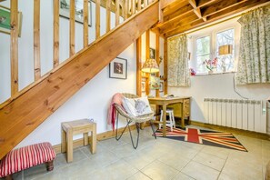 Ein gemütliches Zimmer mit einer Holztreppe, einem Schreibtisch, einem Stuhl, einem Heizkörper und einem Fenster mit Vorhängen.