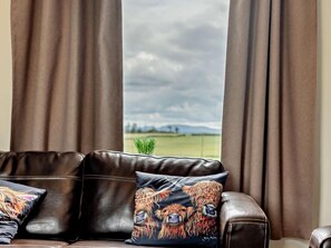A leather sofa with two cushions, one with a dog design, in front of a window with curtains. - 2 Bed in Carluke (oc-95359) (Carluke)