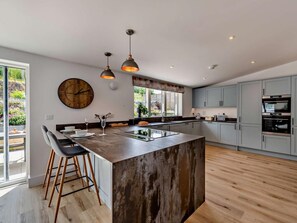 A modern kitchen with a central island, pendant lighting, and a large clock on the wall. - 4 Bed in Bideford (oc-95384) (Westward Ho!)