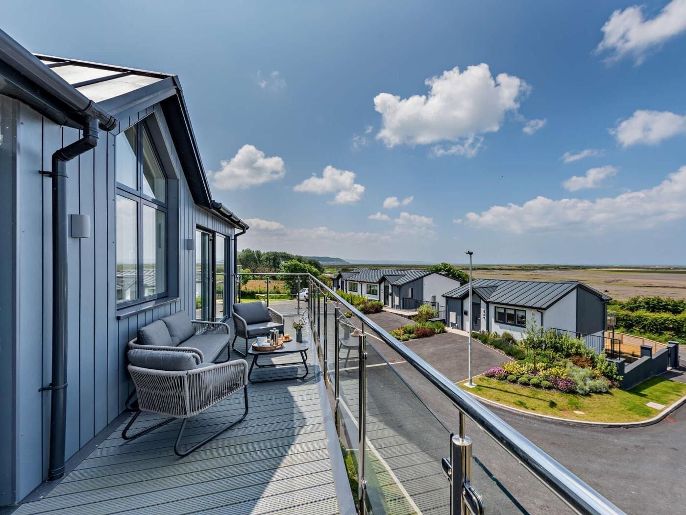 Ein modernes Gebäude mit Balkon, Sitzgelegenheit im Freien und Blick auf eine angelegte Grünfläche.