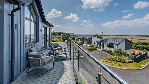 En moderne bygning med balkon, udendørs siddepladser og udsigt over en anlagt have.
