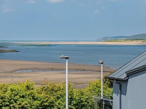 A coastal view with a beach, a building with a sloped roof, and two street lamps. - 4 Bed in Bideford (oc-95384) (Westward Ho!)