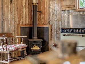 A rustic room with a wood-burning stove, a wooden table with a plaid cushion, and a metal stove with controls. - 1 Bed in Kendal (oc-95349) (Ings)