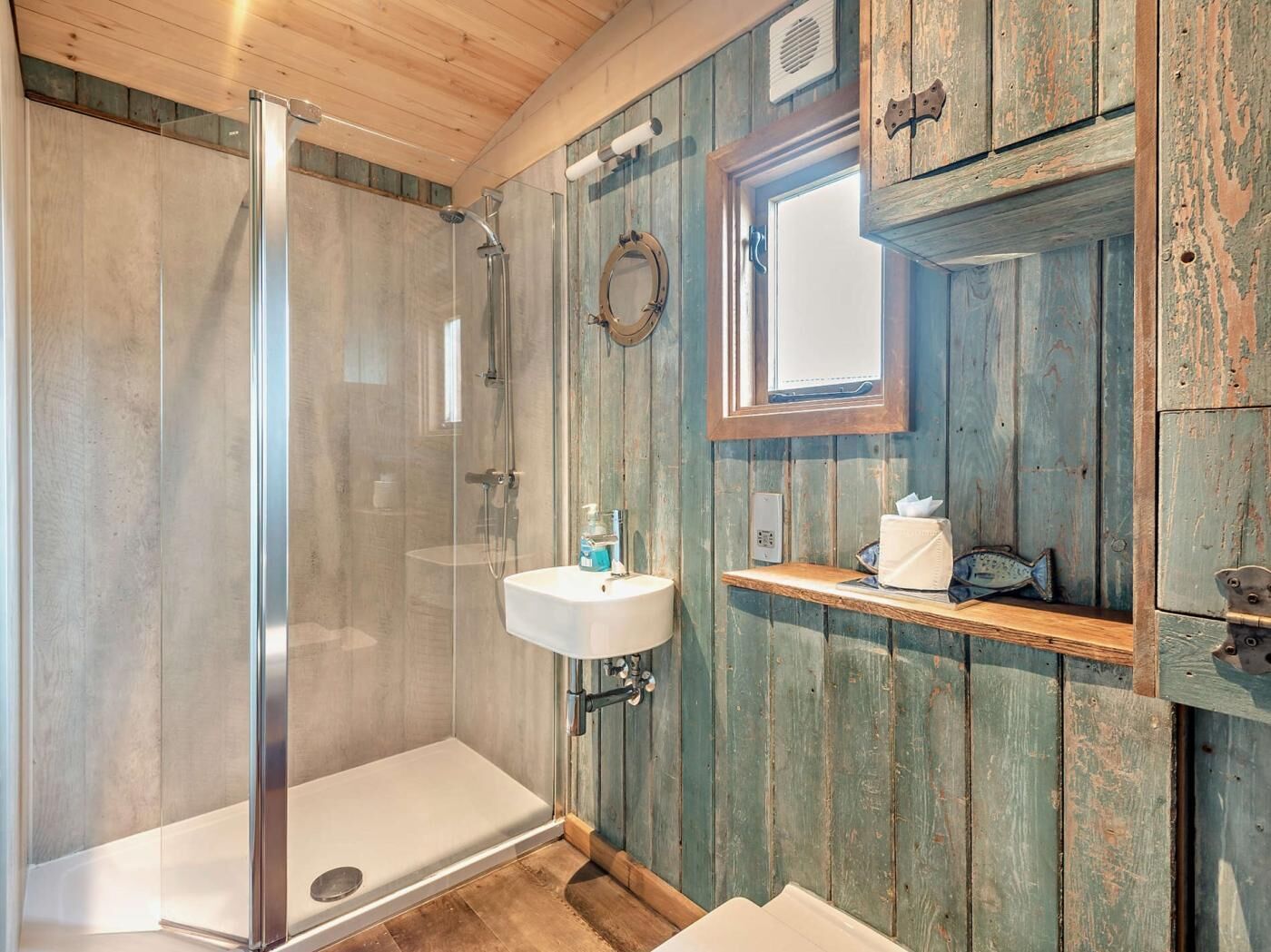 A bathroom with a glass-enclosed shower, a white sink, and wooden walls.