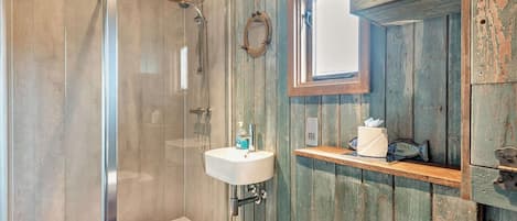 A bathroom with a glass-enclosed shower, a white sink, and wooden walls.