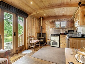 A rustic cabin interior with a wood-paneled kitchen, a fireplace, and a dining area. - 1 Bed in Kendal (oc-95349) (Ings)