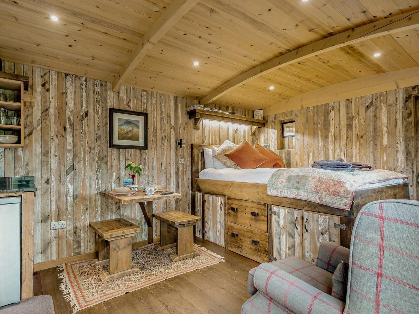 A rustic room with a bunk bed, a small table with a plant, a chair, and a wooden cabinet.