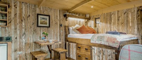 A rustic room with a bunk bed, a small table with a plant, a chair, and a wooden cabinet.
