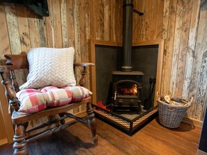 A wooden-framed chair with a plaid cushion and a white knitted throw, positioned in front of a wood-burning stove. - 1 Bed in Kendal (oc-95349) (Ings)
