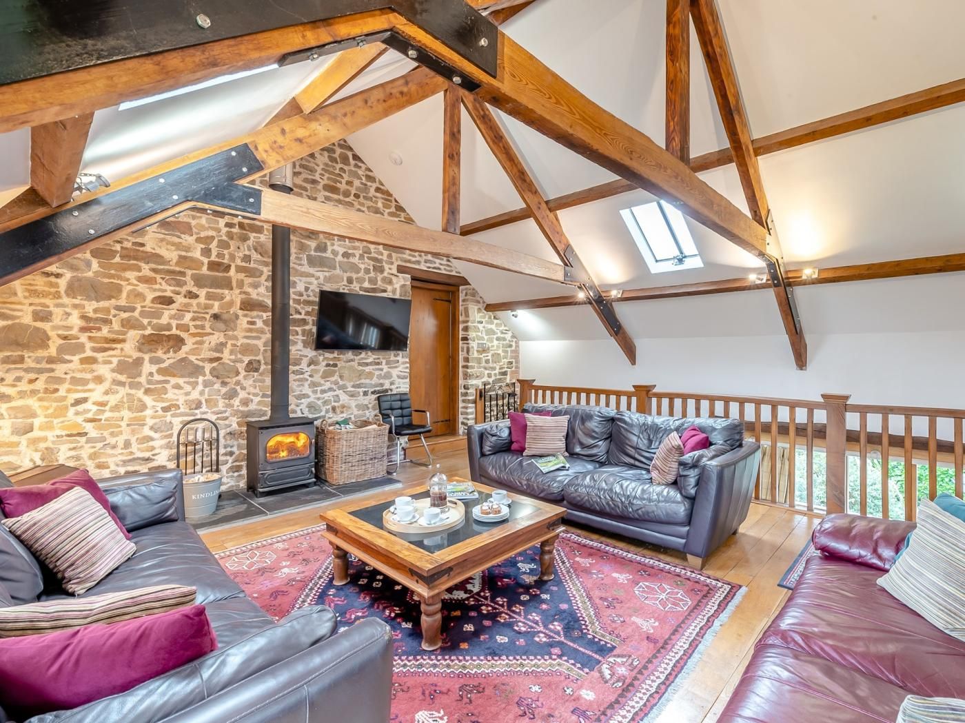 Un salon chaleureux avec un mur en pierre, une cheminée, des canapés en cuir et une structure de plafond en bois.