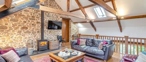 Una sala de estar acogedora con una pared de piedra, chimenea, sofás de cuero y estructura de techo de madera.
