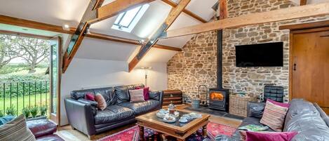 A cozy living room with a stone wall, a fireplace, and a large window overlooking a garden.