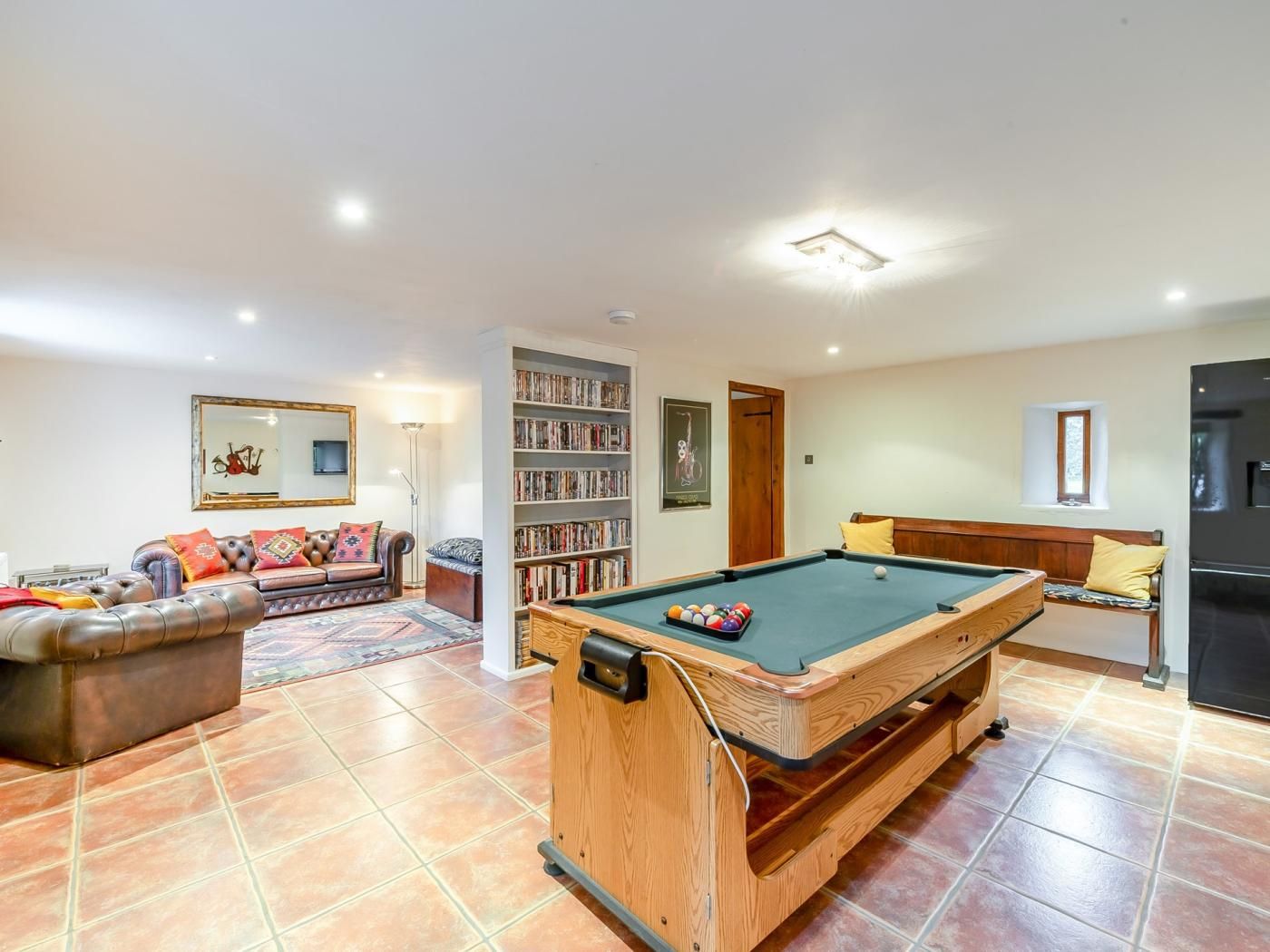 A living room with a pool table, a sofa, a bookshelf, and a dining area.