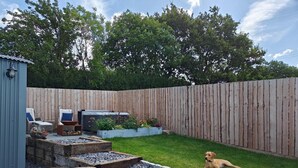 Un patio trasero con cerca de madera, una parrilla, mobiliario exterior y un perro.