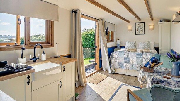 Un dormitorio con un ventanal grande, una cama con edredón estampado, una mesita de noche y vistas al verdor exterior.