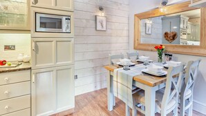 A dining area with a wooden table, white chairs, a white cabinet with a microwave, and a wall-mounted mirror. - 2 Bed in Carnforth (oc-95452) (Kirkby Lonsdale)