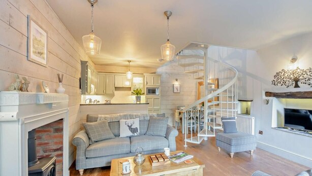A modern living room with a fireplace, a sofa set, a coffee table, and a spiral staircase. - 2 Bed in Carnforth (oc-95452) (Kirkby Lonsdale)