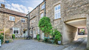 A stone building with a courtyard, outdoor seating, and a car parked in the background. - 2 Bed in Carnforth (oc-95452) (Kirkby Lonsdale)