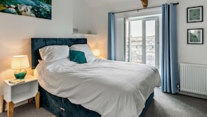 Ein Schlafzimmer mit Bett, Nachttisch, einem Fenster mit Vorhängen und einem Bild an der Wand.