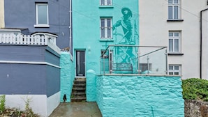 Ein Gebäude mit einer türkisblauen Fassade, einer sichtbaren Tür und einer Treppe, die zum Eingang führt.