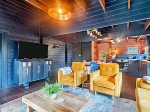 Ein modernes Wohnzimmer mit Fernseher, Sofa, Couchtisch und einer Küche im Hintergrund.