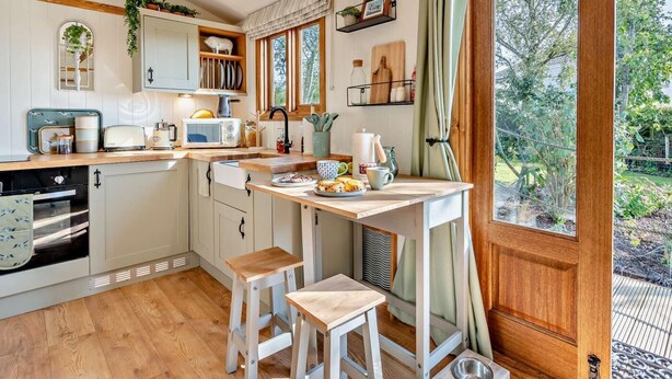 A kitchen with wooden beams, a window with curtains, a sink, a microwave, and a dining area with stools. - 1 Bed in Broxburn (oc-95472) (Broxburn)