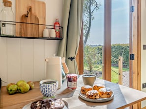 Ein Esstisch mit Äpfeln, einer Kaffeetasse, einem Teekännchen, Marmelade und Gebäck.