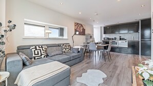 Ein modernes Wohnzimmer mit grauem Sofa, einem Essbereich und einer Küche mit dunklen Schränken.